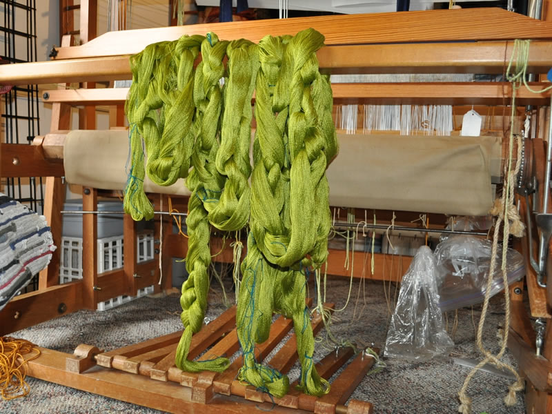 Image of yarn hanging across the front beam of a floor loom.